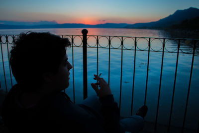 Man holding cigarette while sitting against sea during sunset