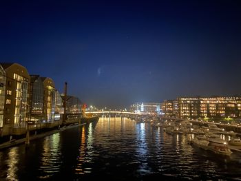 Illuminated buildings by river against sky at night