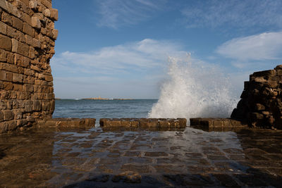 Sea waves splashing on rocks against sky