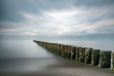 Row of wooden posts in sea against cloudy sky during foggy weather