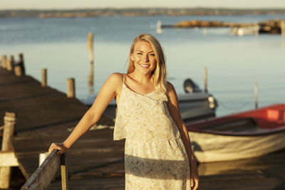 Portrait of smiling blond woman standing by railing at jetty
