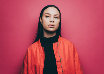 Portrait of confident woman wearing orange jacket over pink background