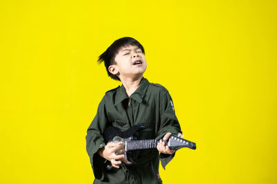 Young man looking away while standing against yellow background