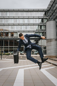 Businessman jumping mid-air while holding briefcase in front of building
