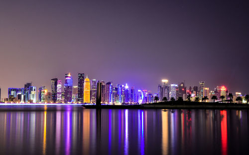 Illuminated buildings by river against sky at night