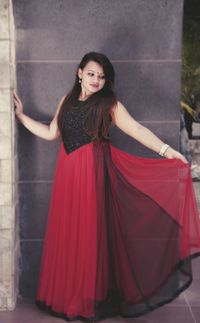 Portrait of beautiful young woman standing against red wall