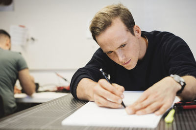 Engineer planning on paper at table with colleague in background