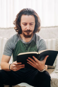 Mid adult man sitting on sofa at home reading a book