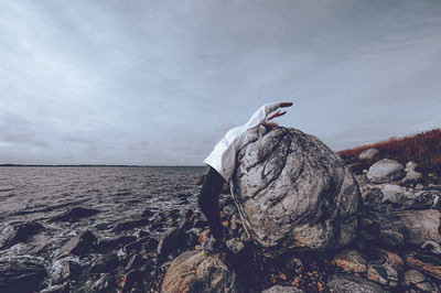 Man standing on rock by sea against sky