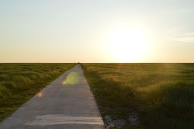 Road on grassy field against sky during sunset