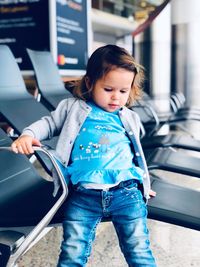 Cute baby girl standing by chair