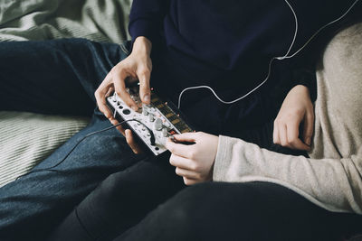 Midsection of friends using sound mixer while sitting at bedroom