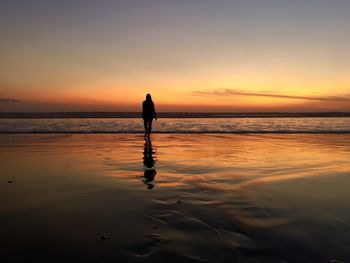 Silhouette woman on beach against sky during sunset