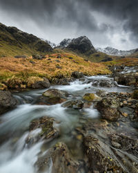 Stream flowing through rocks against sky