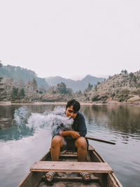 Man smoking while sitting in boat on lake against clear sky