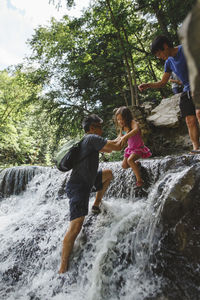 Uncle carrying girl while moving down in waterfall at forest