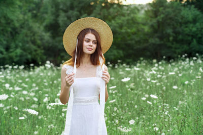 Portrait of young woman wearing hat standing against plants