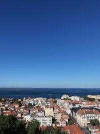 High angle view of townscape by sea against clear blue sky