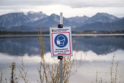 Warning sign by lake against sky