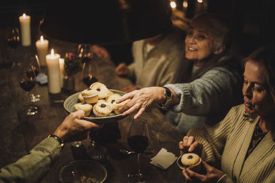 Senior woman taking cupcake from plate during dinner party