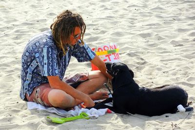 Woman with dog sitting on sand at beach
