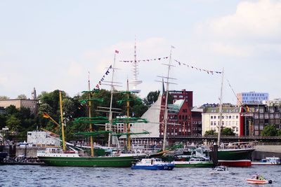 Sailboats moored on river by city against sky