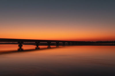 Silhouette bridge over the calm river against a romantic october sky during sunset.