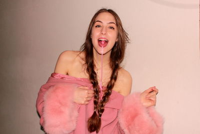 Portrait of young woman showing bubble gum in mouth against wall