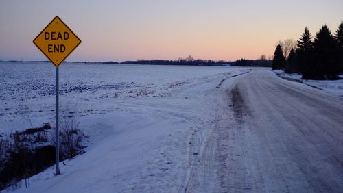 Road sign on snow covered landscape against sky