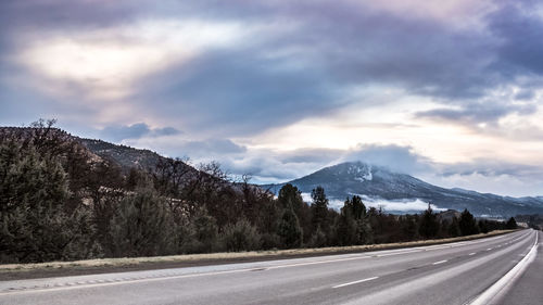 Road by trees and mountains against sky