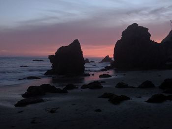 Rock formation on beach against sky during sunset