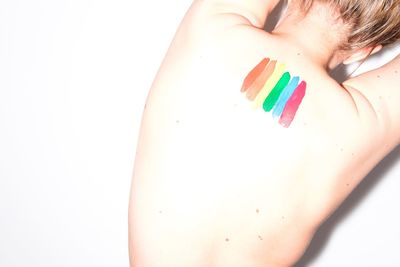 Rear view of shirtless woman with colorful paints on her back by white wall