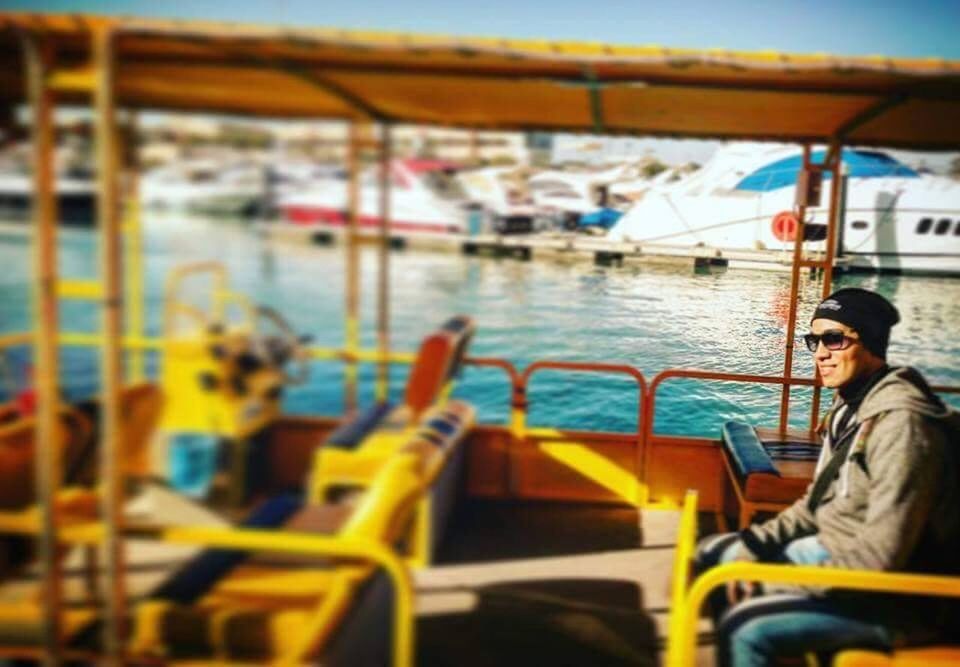 nautical vessel, water, transportation, one person, sitting, mode of transportation, young adult, sea, portrait, day, side view, adult, leisure activity, focus on foreground, holding, casual clothing, travel, outdoors