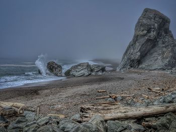 Driftwood on beach against boulders and foggy sky