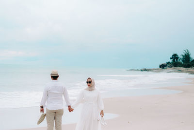 Rear view of woman standing at beach against sky