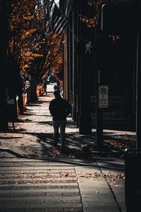 Rear view of man walking on footpath in city