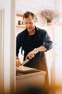 Mature man cutting cheese on board at kitchen counter