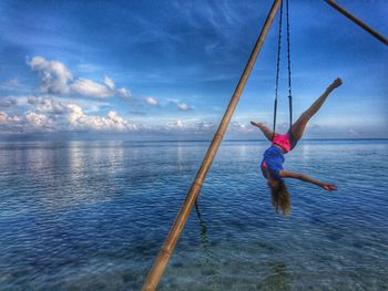 Full length of woman hanging over sea against cloudy sky