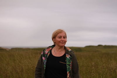 Portrait of smiling young woman standing on field against sky