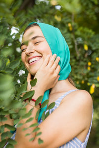 Smiling woman holding hat while standing against plants