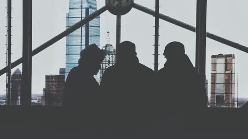 Rear view of silhouette people standing against window in city