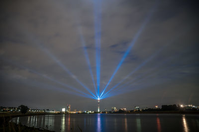 Illuminated city by river against sky at night