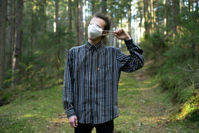 Full length of man standing in forest taking off his mask 