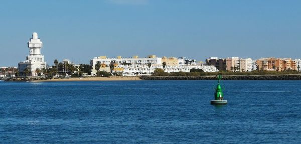 Sailboats in sea by buildings against clear sky