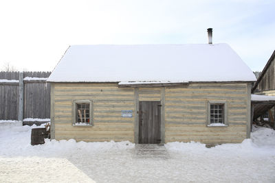 House on snow covered field by building against sky