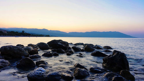 Rocks on sea shore against sky during sunset