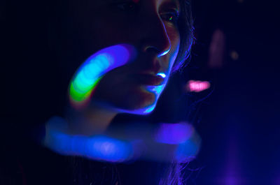 Close-up of young woman against illuminated lighting equipment