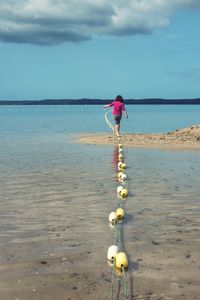 Girl walking by buoys on shore at beach against sky