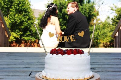 Close-up of wedding cake with bridegroom sitting on plank in background