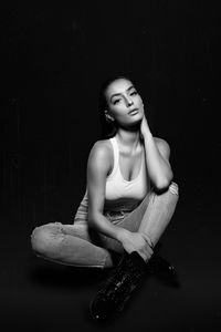 Full length of young woman sitting against black background